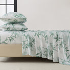 Bed with green leaf patterned bedding and pillows on a neutral background
