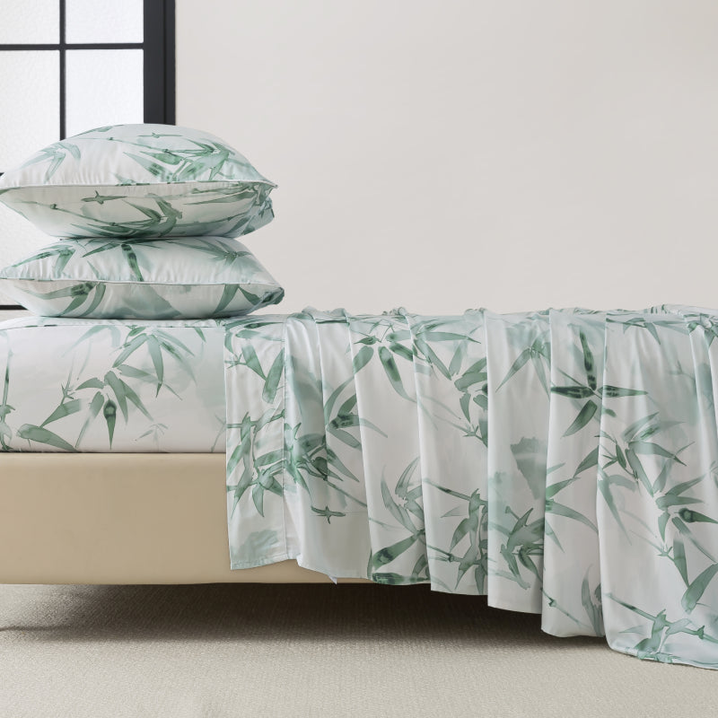 Bed with green leaf patterned bedding and pillows on a neutral background